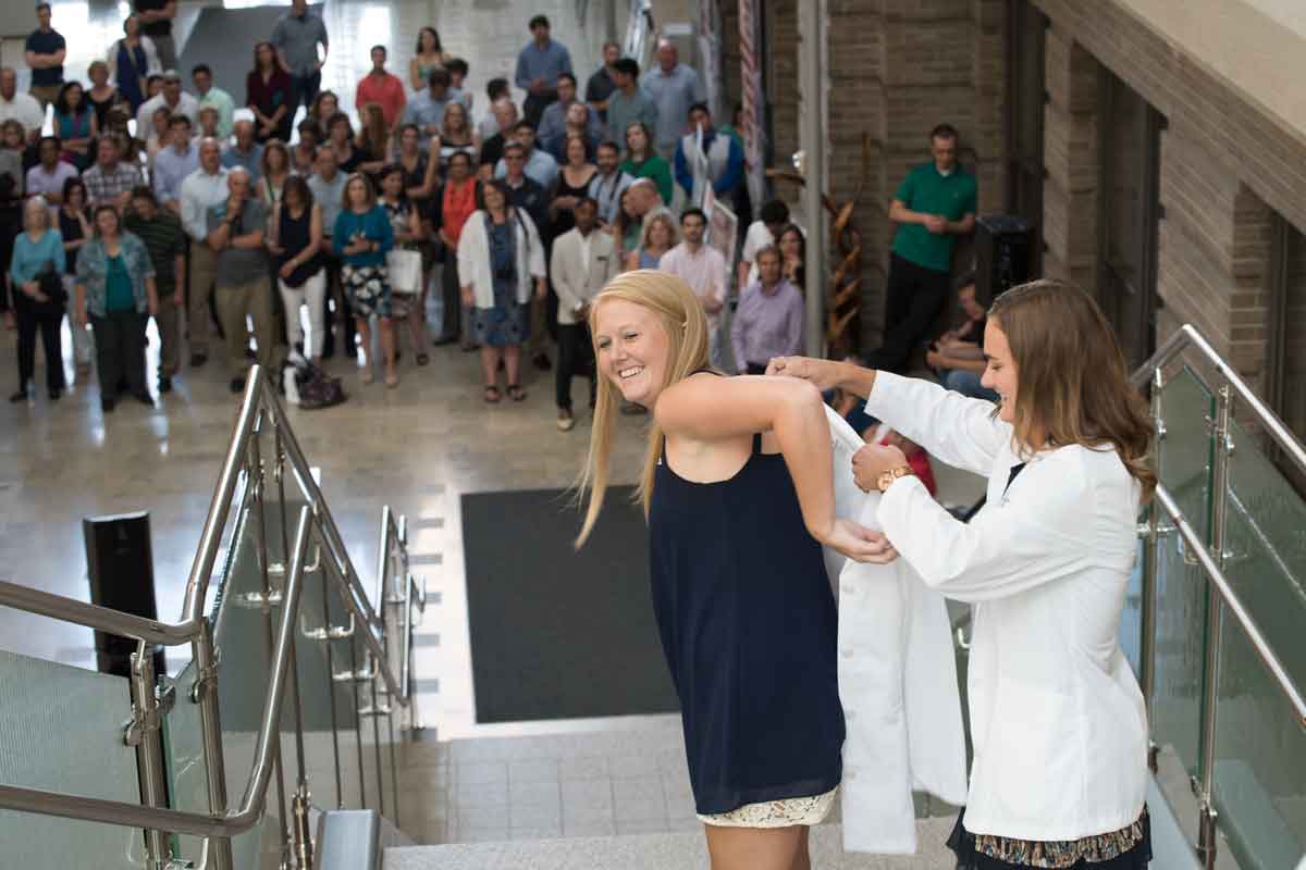 Second-year physical therapy student Torey Bird helps first-year student Krista Zerrusen into a white coat at the ceremony on the Medical Campus.