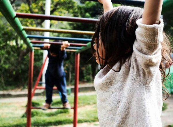 Two children cross colorfully painted monkey bars at a park