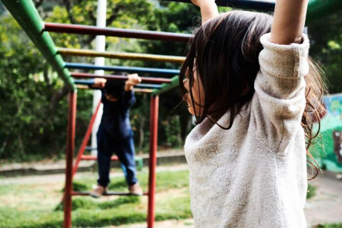 Two children cross colorfully painted monkey bars at a park