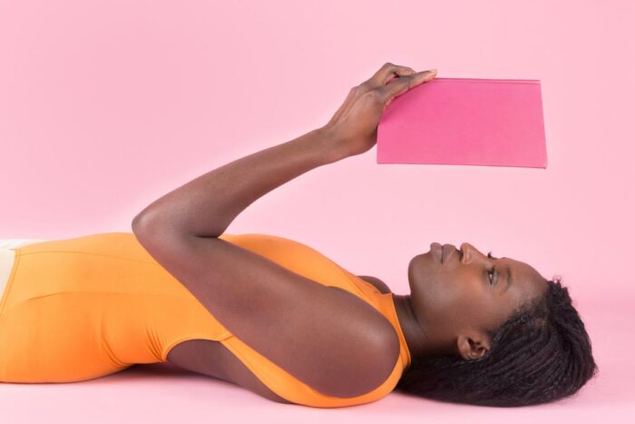 A woman lies are on her back reading a book