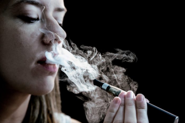 A woman exhales a cloud of vapor from an e-cigarette