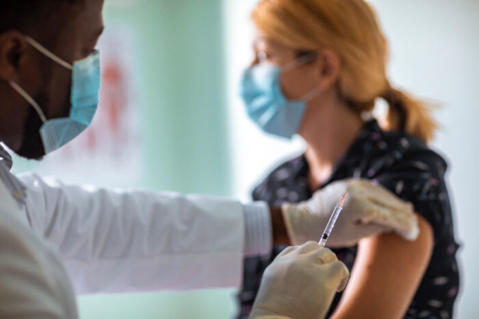 A woman wearing a mask prepares to receive a vaccination in her upper arm
