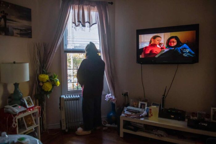 A teen stands at the living room window of her home, looking outside