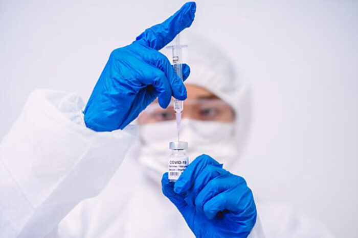 A person wearing PPE draws a vaccination dose from a small glass vial