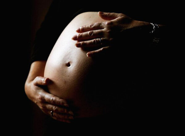 Dark photo showing a woman's illuminated pregnant belly