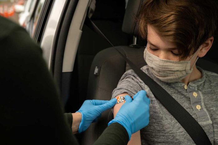 A person wearing a mask getting a bandage on their upper arm after receiving a COVID-19 vaccine