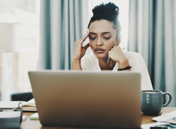 A woman sitting at a computer rests her chin on her hand and holds her temple