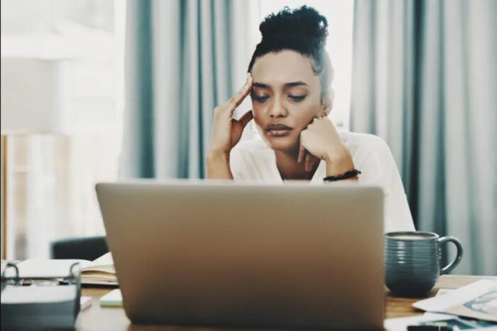 A woman sitting at a computer rests her chin on her hand and holds her temple