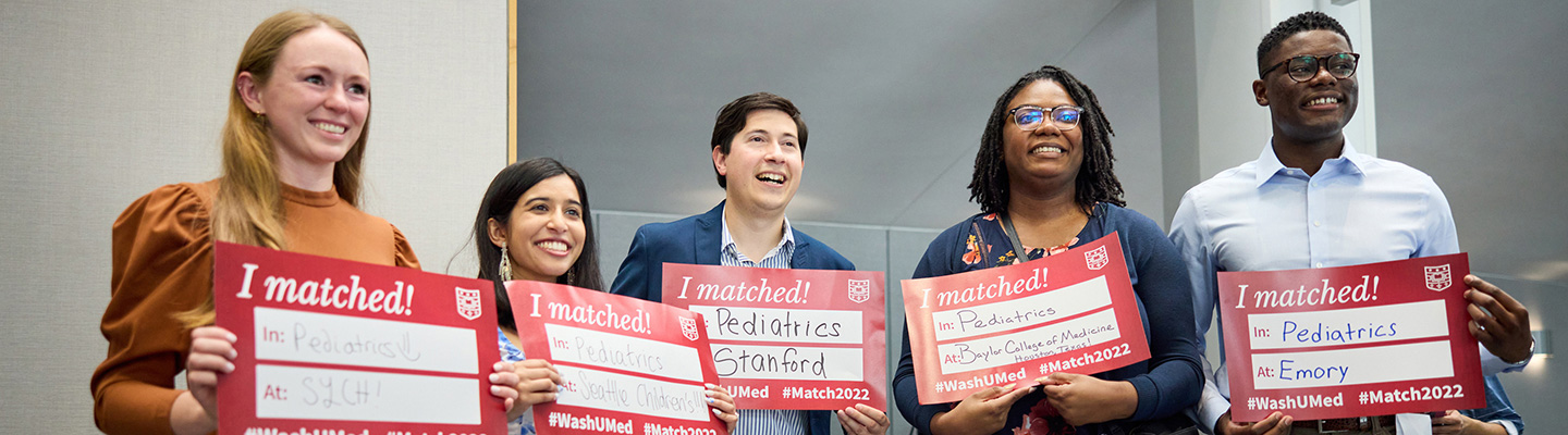 Five medical students at Match Day hold red "I matched!" signs that say where they matched for residency, and in what specialty.