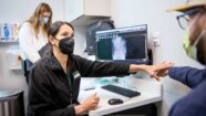 Devyani M. Hunt, MD, a professor of orthopedic surgery and medical director of the Living Well Center, talks with patient Zach Wood about pain issues. A computer monitor on the desk beside Dr. Hunt displays a spinal scan.