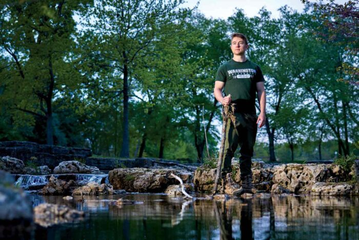 Medical student Joshua Perez-Cruet stands on the boulder in the middle of a calm stream surrounded by leafy trees. Perez-Cruet and fellow medical students nationally are calling for more education on climate change.