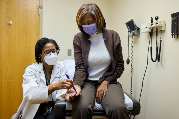 Study volunteer Stephanie Griffin is seated in an exam room as Dr. Lenise Cummings-Vaughn, runs a neurological test for a study. Both women are Black.