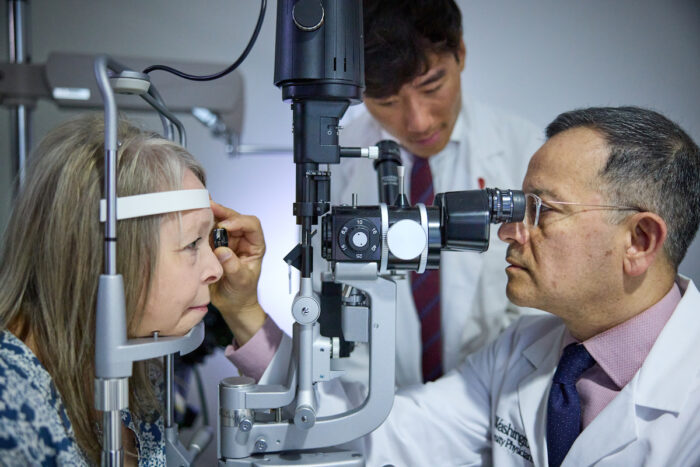 ophthalmologist examines patients eyes while medical student observes