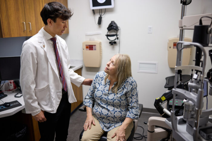 a standing medical student talks with a sitting patient in an exam room