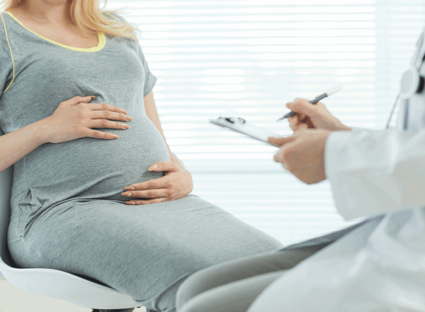 Pregnant woman in gray dress talking to doctor in white coat