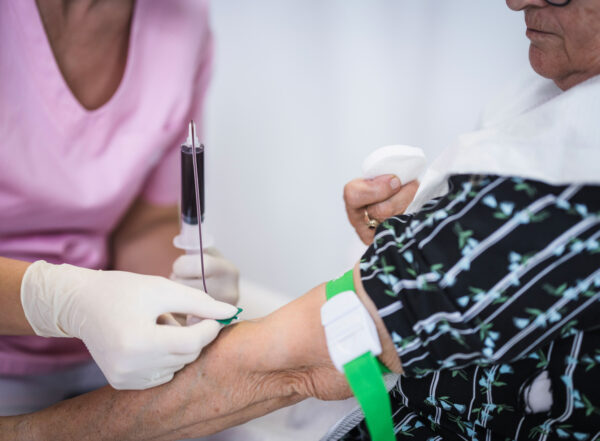 A woman draws blood from the arm of an older woman.