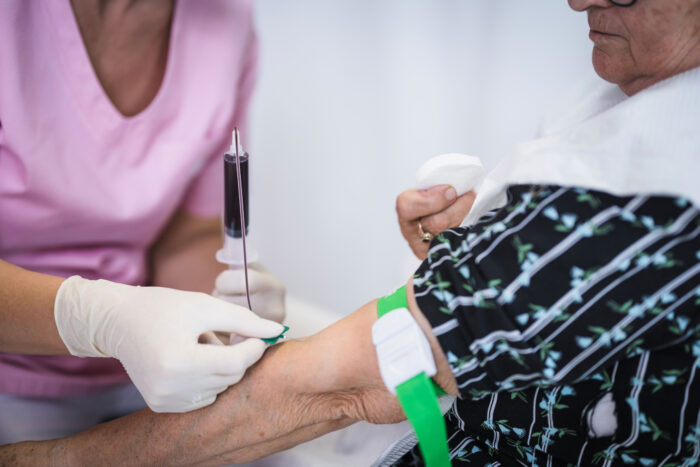 A woman draws blood from the arm of an older woman.