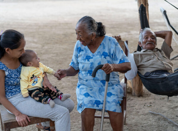 Older Peruvian woman with a cane smiles at a baby sitting on a young woman's lap. An older man relaxes behind them.