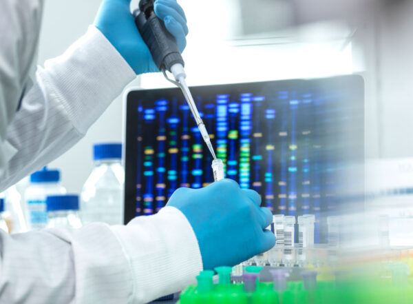 Gloved hands pipette liquid from a vial in front of a screen with colored lines.