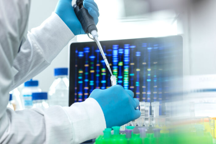 Gloved hands pipette liquid from a vial in front of a screen with colored lines.