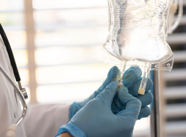 A person wearing a white medical coat and blue gloves prepares an IV drip bag.