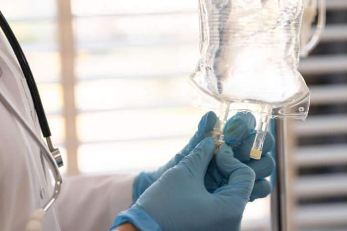 A person wearing a white medical coat and blue gloves prepares an IV drip bag.