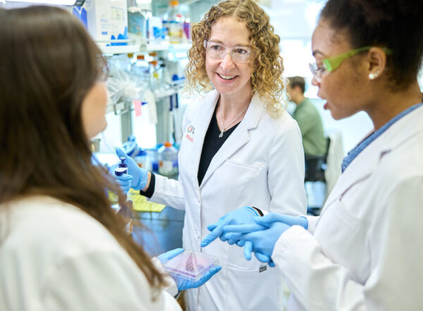 Kate Wardenburg (left), an MD/PhD student in the Medical Scientist Training Program, Christina Stallings, PhD (center), and Ananda Rankin, a graduate student in the Roy and Diana Vagelos Division of Biology & Biomedical Sciences, wearing white coats in the lab