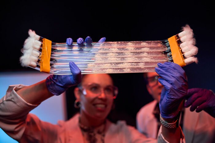 Woman in white coat examining powder in white tubes.