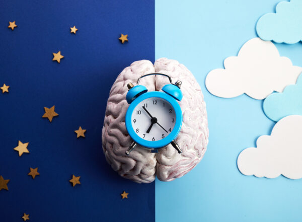 Alarm clock resting on a brain with a split background of night sky with stars and day sky with clouds