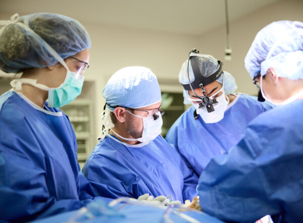 An image of four surgeons wearing protective clothing performing a procedure for plastic and reconstructive surgery.