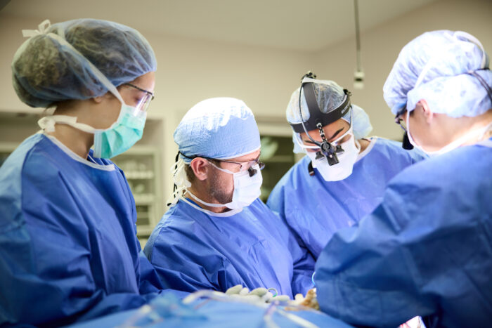 An image of four surgeons wearing protective clothing performing a procedure for plastic and reconstructive surgery.