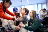 Student measures little boy's waist while his mom holds his hand.