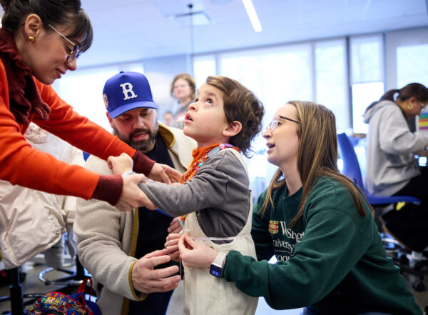 Student measures little boy's waist while his mom holds his hand.