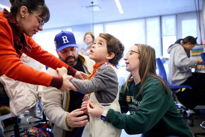 Student measures little boy's waist while his mom holds his hand.