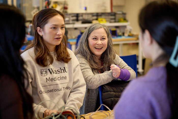 Professor smiles as she listens to two students converse about their project.