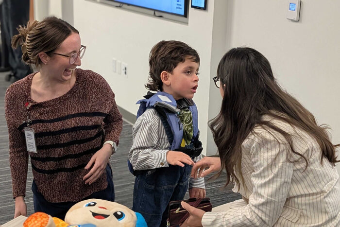 Little boy tries on vest while his mom and a student watch.