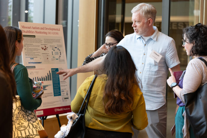 Man in blue shirt points to poster, sharing information about its contents to five attendees.