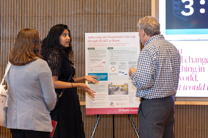 Woman in black dress presents poster to two attendees.