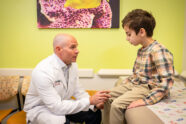 Male physician in exam room with young patient, examining his knee