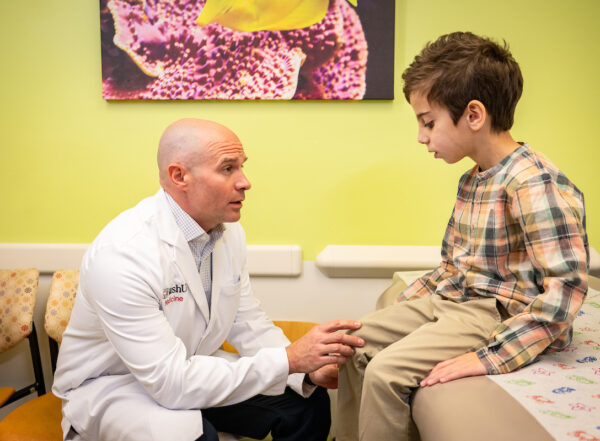 Male physician in exam room with young patient, examining his knee