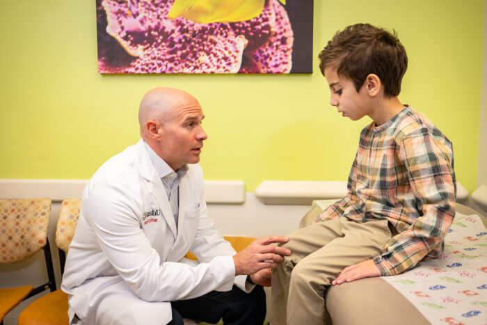 Male physician in exam room with young patient, examining his knee