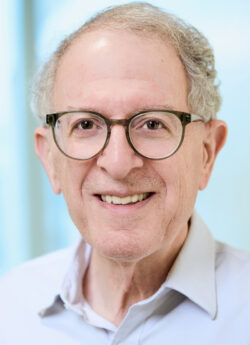 Headshot of male researcher who is smiling and wearing glasses and a white shirt