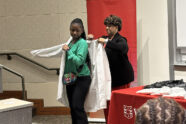 Woman standing behind high school girl, helping her into a medical white coat