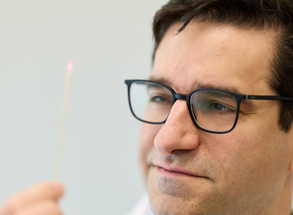 A person wearing glasses holds a thin stick with a small pink tip, looking at it intently.