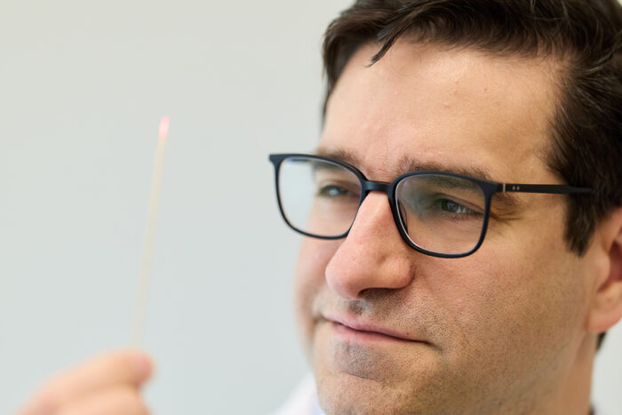 A person wearing glasses holds a thin stick with a small pink tip, looking at it intently.