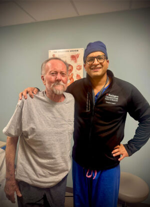 Man in gray shirt and male in surgical cap and black zip up top.