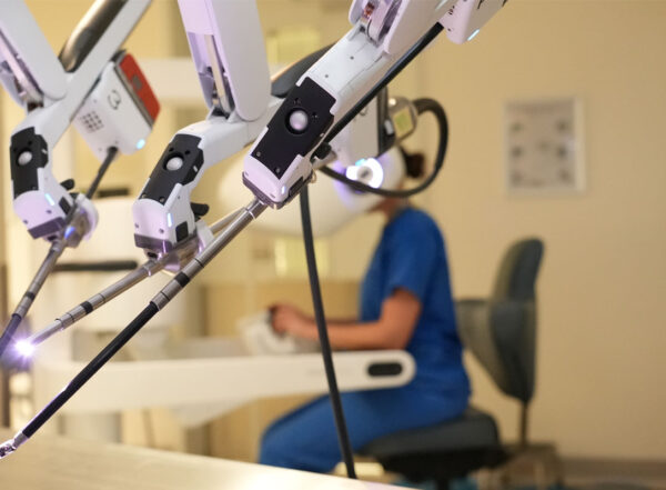 Surgical robot controlled by doctor in scrubs in the background.