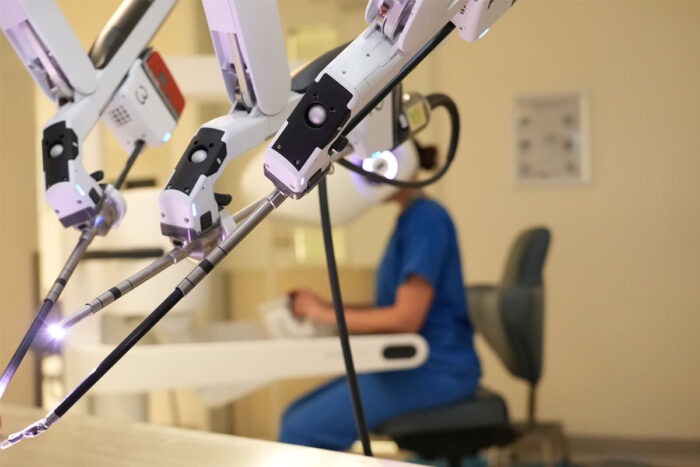 Surgical robot controlled by doctor in scrubs in the background.
