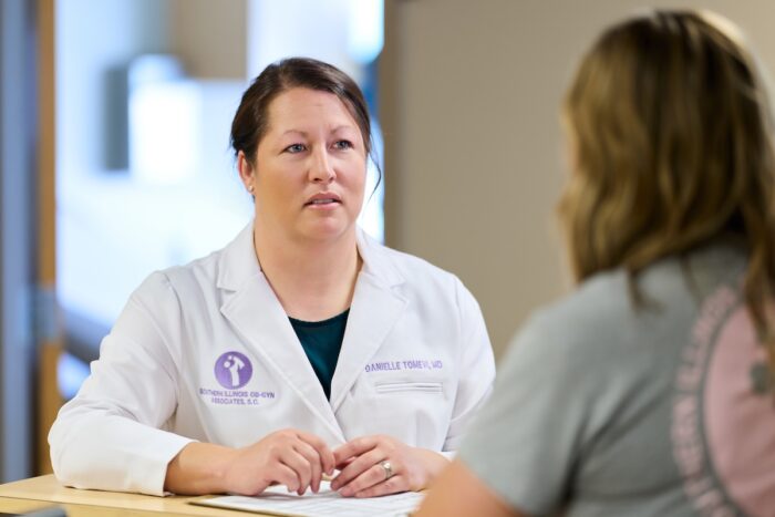 A healthcare professional in a white coat engages in a consultation with a patient at a desk.