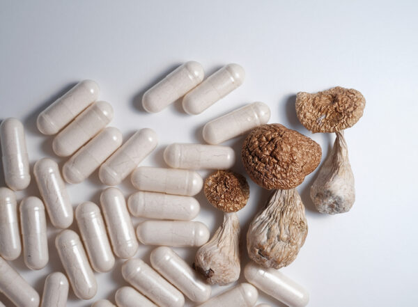 White pills and psilocybin mushrooms on white studio background, close up.